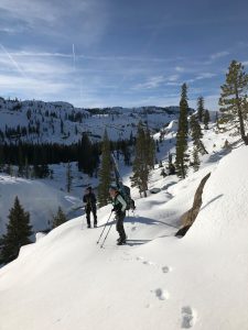 Ski-clad snow surveyors stand on snowy bank in Yosemite under blue skies